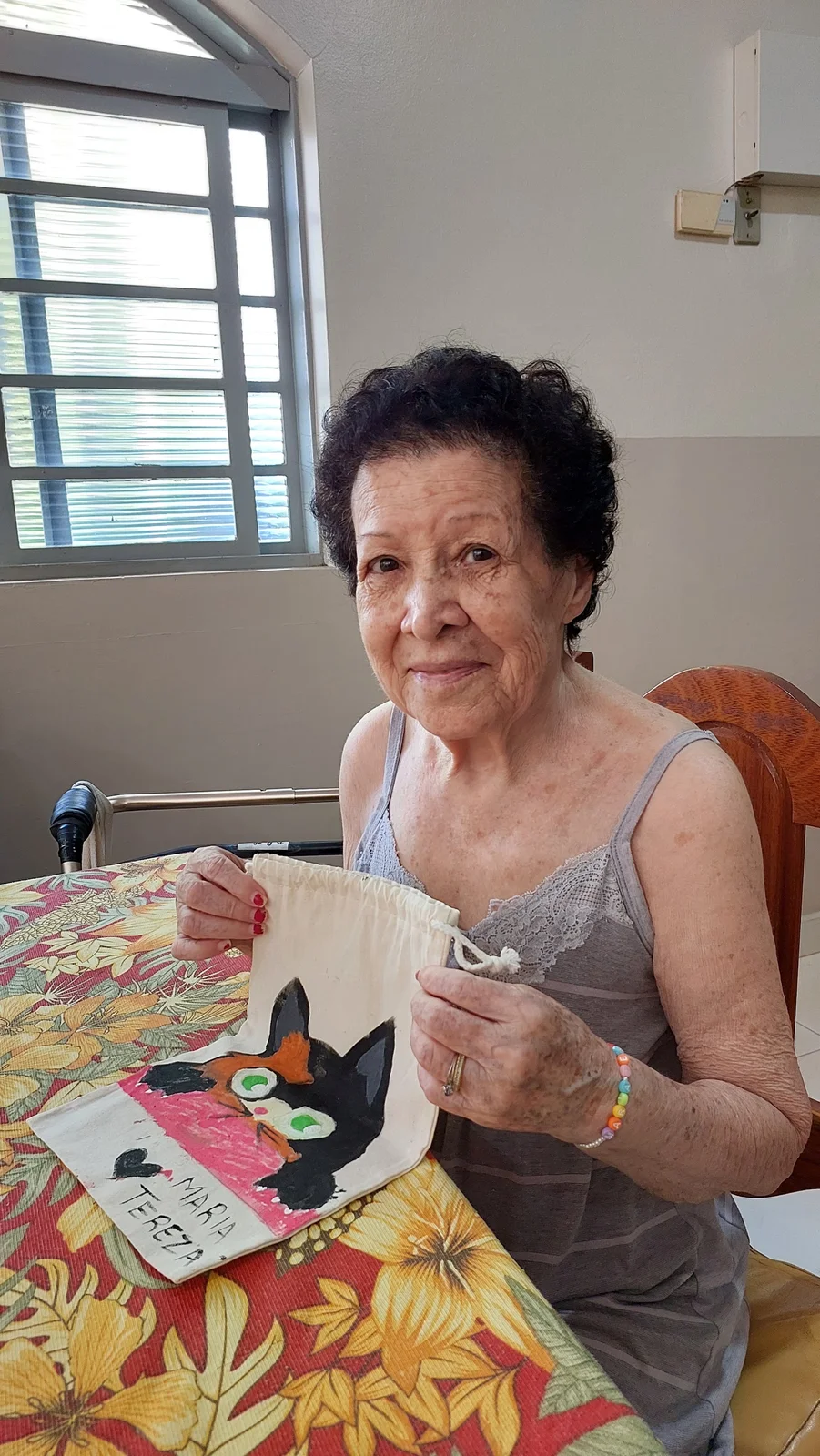 Dona Maria Tereza exibindo bolsa artesanal com desenho de gatinho