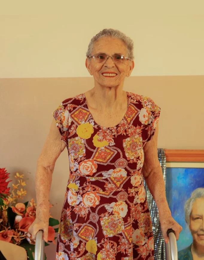 Dona Maria Giselia em pé com andador e vestido estampado